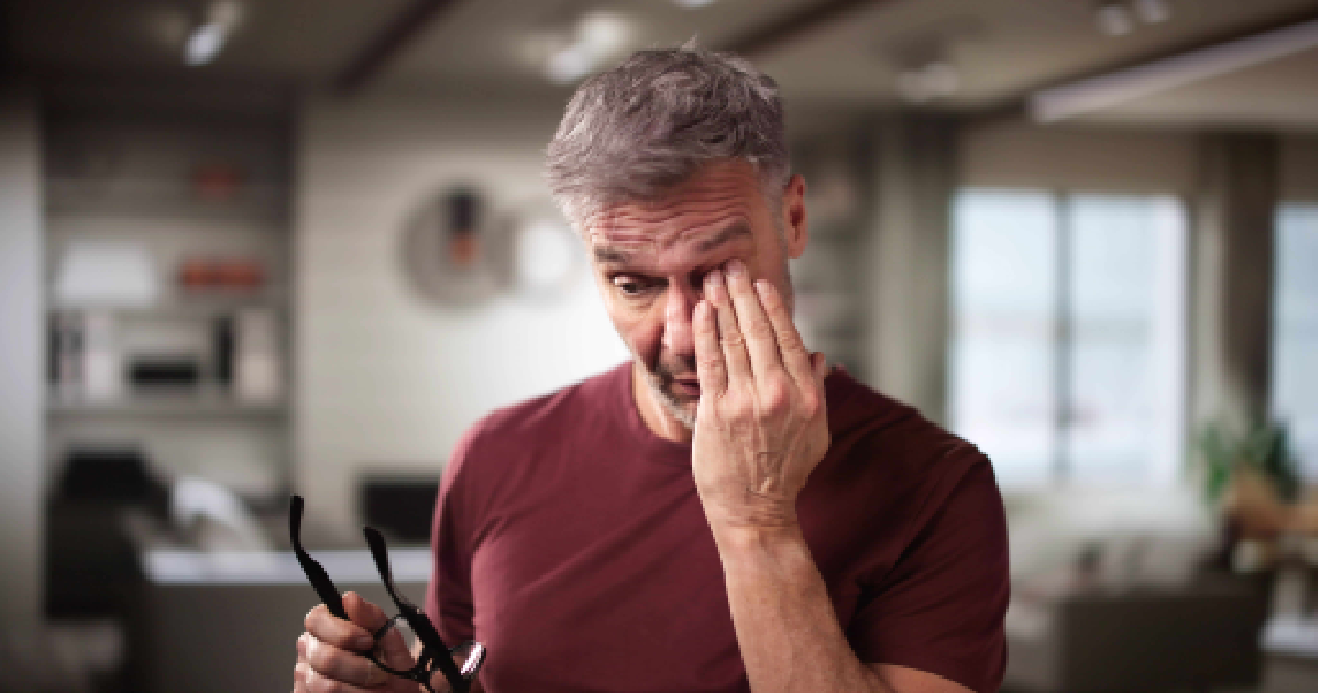 Middle-aged man rubbing his irritated eye while holding eyeglasses, showing symptoms of dry eye discomfort in Glenview, IL